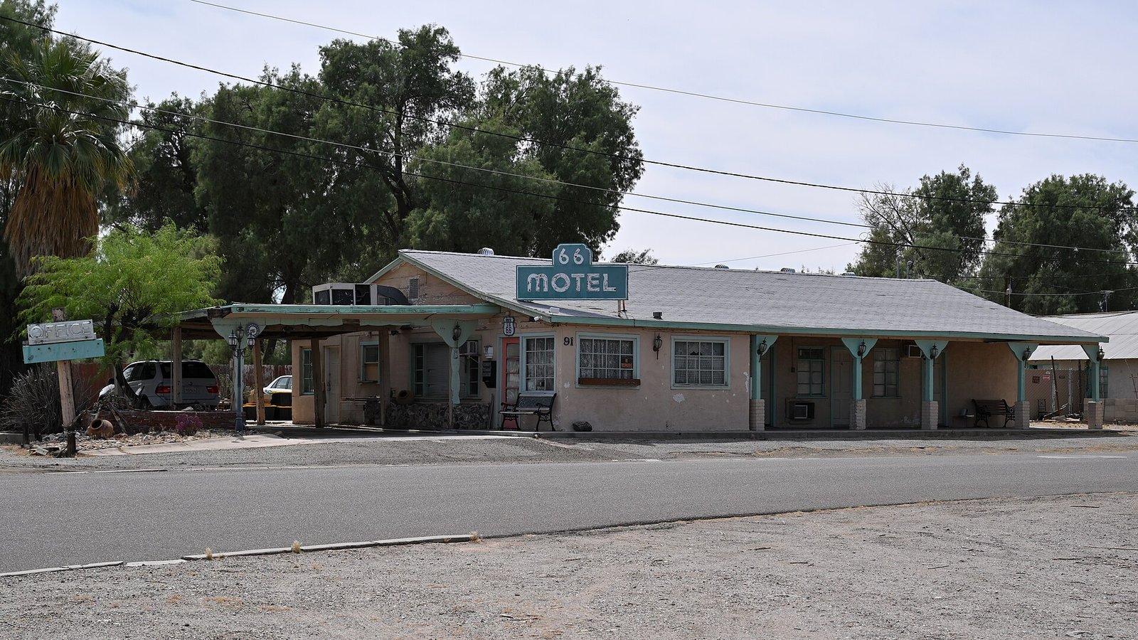 A classic single-storey roadside motel on Route 66 in Needles, California, its room doors opening onto the front parking area