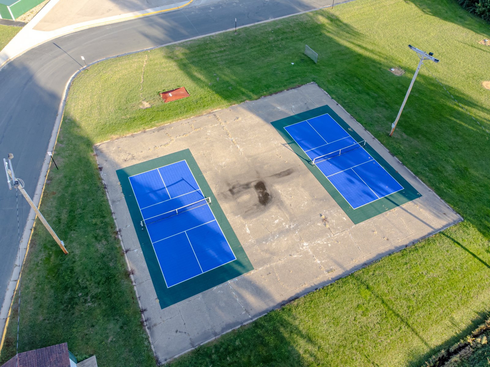 Aerial view of two blue outdoor pickleball courts with white lines and nets, showing the non-volley zone next to each net.